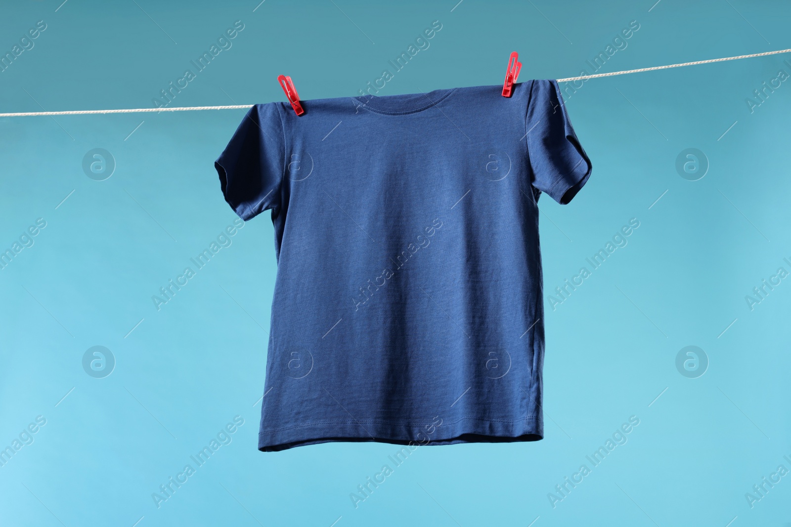 Photo of One t-shirt drying on washing line against light blue background