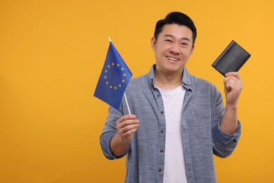 Photo of Immigration. Happy man with passport and flag of European Union on orange background, space for text