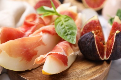 Tasty melon, jamon and figs served on wooden board, closeup