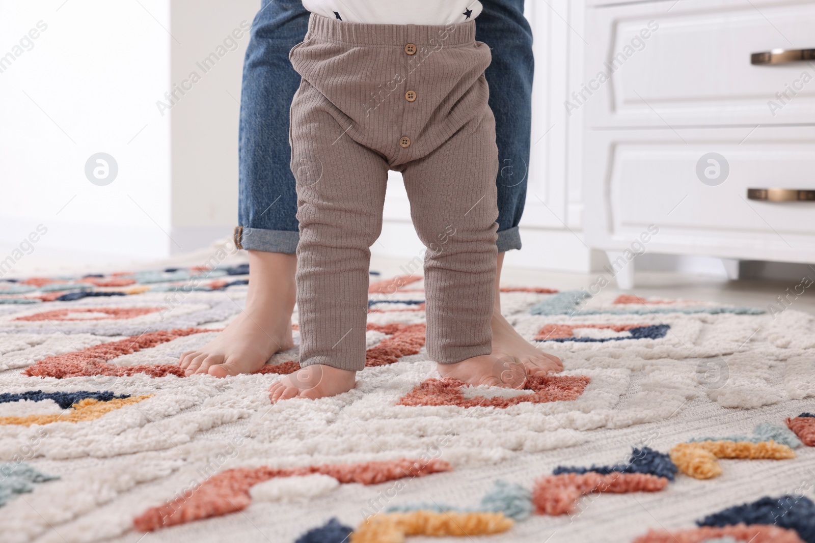 Photo of Mother supporting her baby son while he learning to walk on carpet at home, closeup