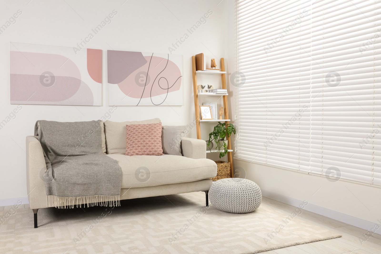 Photo of Stylish room interior with comfortable sofa, wooden shelf and pillows