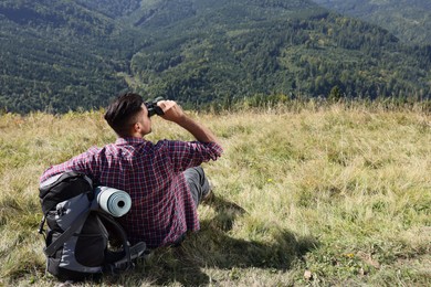 Tourist with hiking equipment looking through binoculars in mountains, back view
