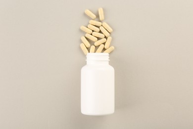 Bottle and vitamin capsules on light background, top view