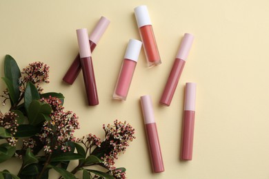 Photo of Different lip glosses and flowers on pale yellow background, flat lay