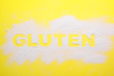 Word Gluten written with flour on yellow background, top view