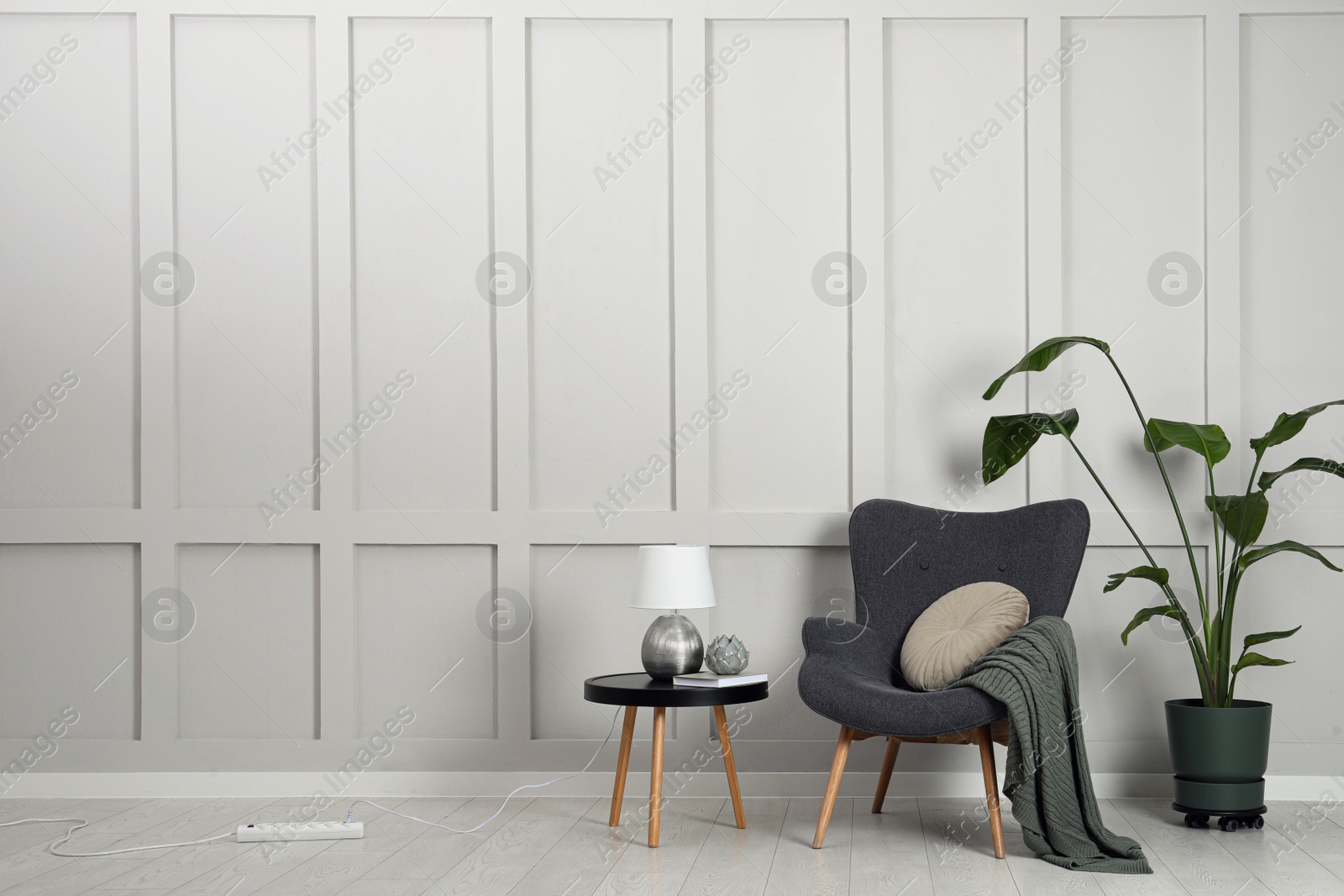 Photo of Comfortable armchair, table with lamp and houseplant near light grey wall in room, space for text. Interior design