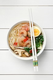 Photo of Tasty ramen with shrimps in bowl and chopsticks on white wooden table, top view