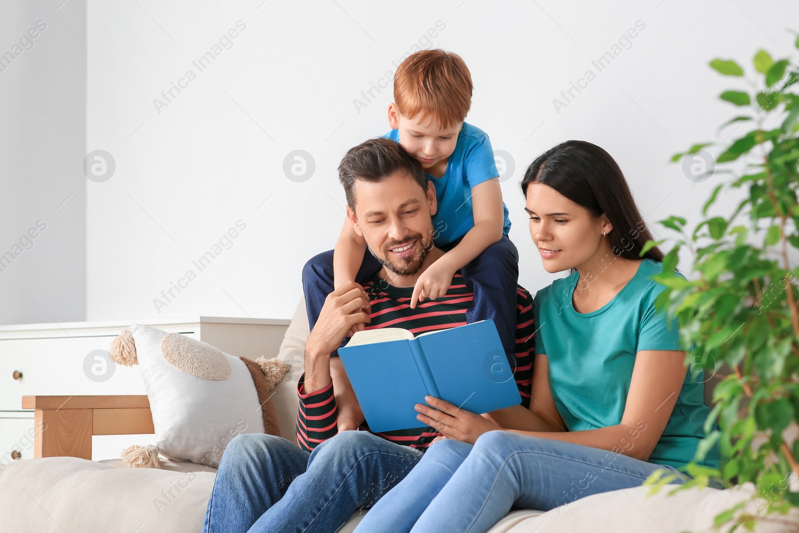 Photo of Happy family reading book together on sofa in living room at home