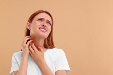 Photo of Suffering from allergy. Young woman scratching her face on beige background, space for text