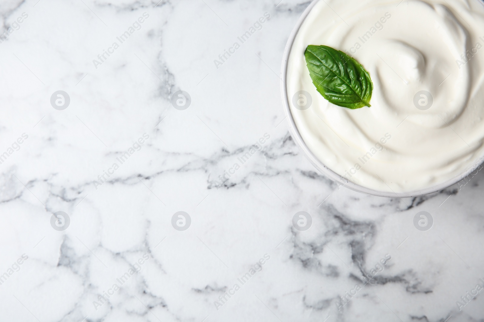 Photo of Bowl of fresh sour cream with basil on white marble table, top view. Space for text