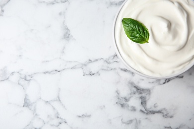 Bowl of fresh sour cream with basil on white marble table, top view. Space for text