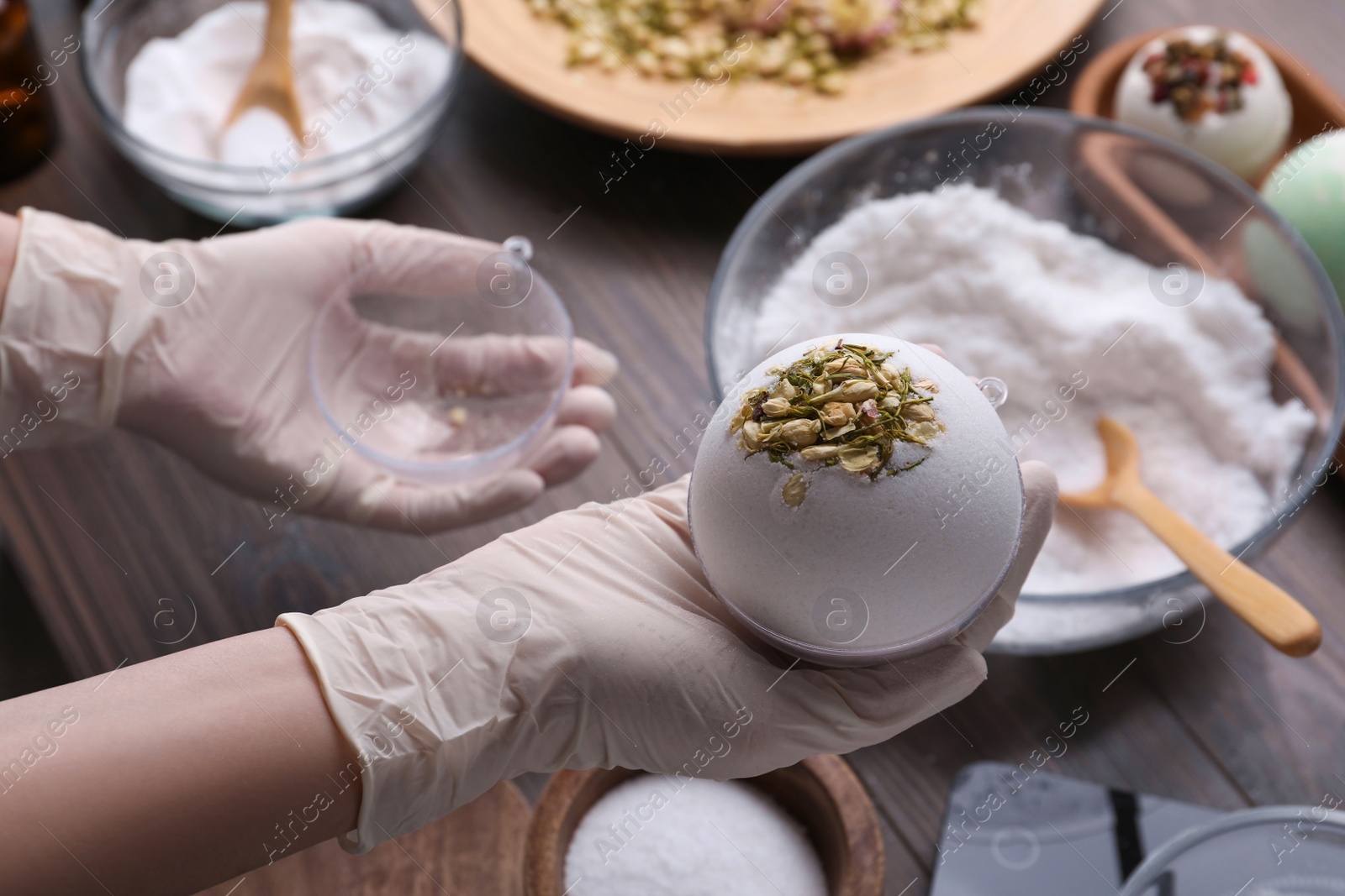 Photo of Woman in gloves making bath bomb at wooden table, closeup