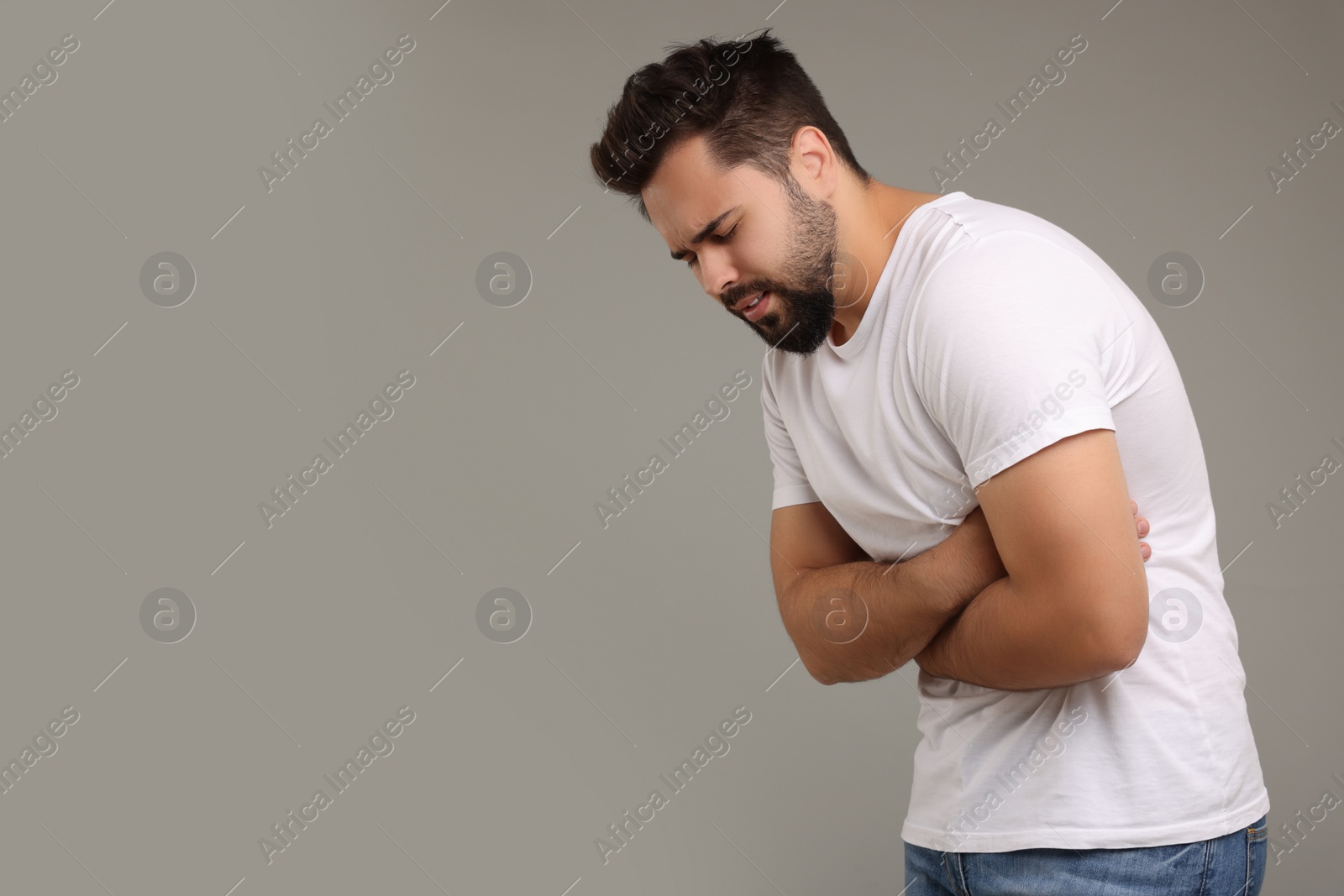 Photo of Young man suffering from stomach pain on light grey background. Space for text