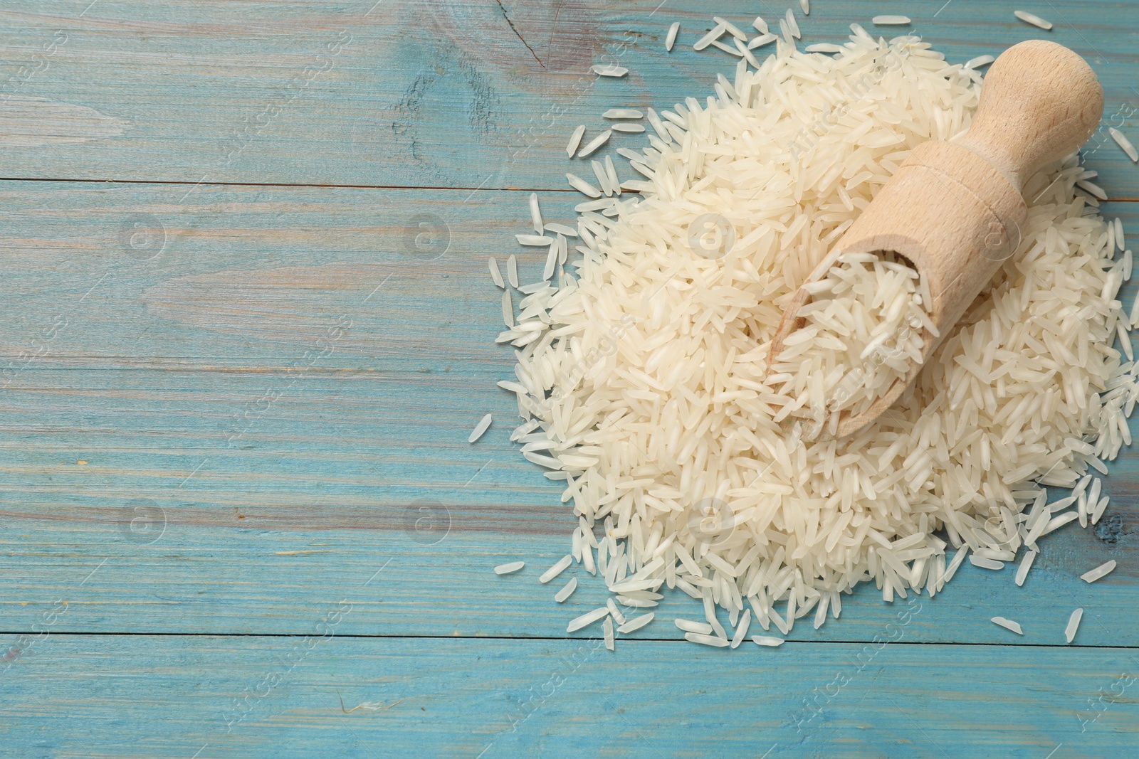 Photo of Raw basmati rice and scoop on light blue wooden table, top view. Space for text