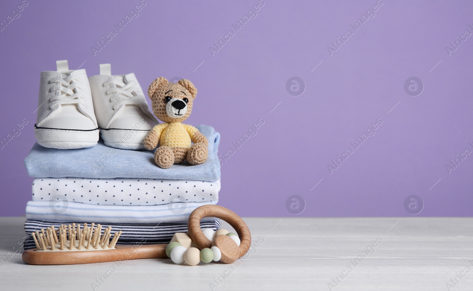 Photo of Children's shoes, stack of clothes and toys on white wooden table. Space for text