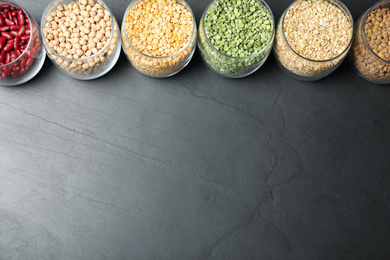 Photo of Glass jars with different types of groats on black table, flat lay. Space for text