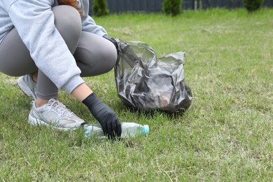 Photo of Woman with trash bag picking up plastic bottle outdoors, closeup. Recycling concept