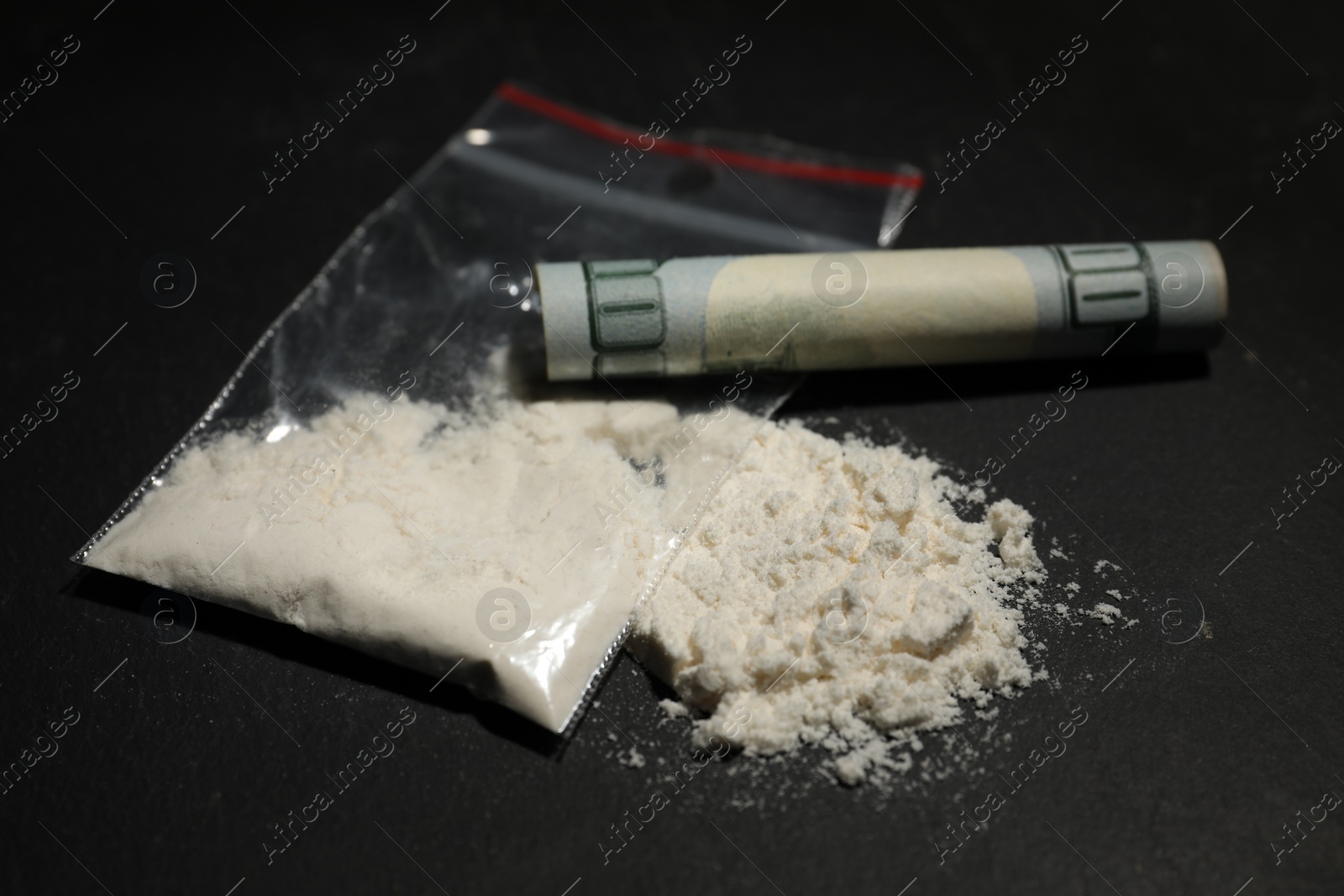 Photo of Drug addiction. Plastic bag with cocaine and rolled dollar banknote on grey textured table, closeup