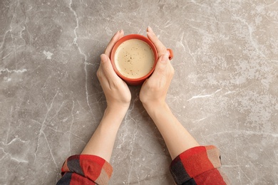 Young woman with cup of delicious hot coffee on table, top view