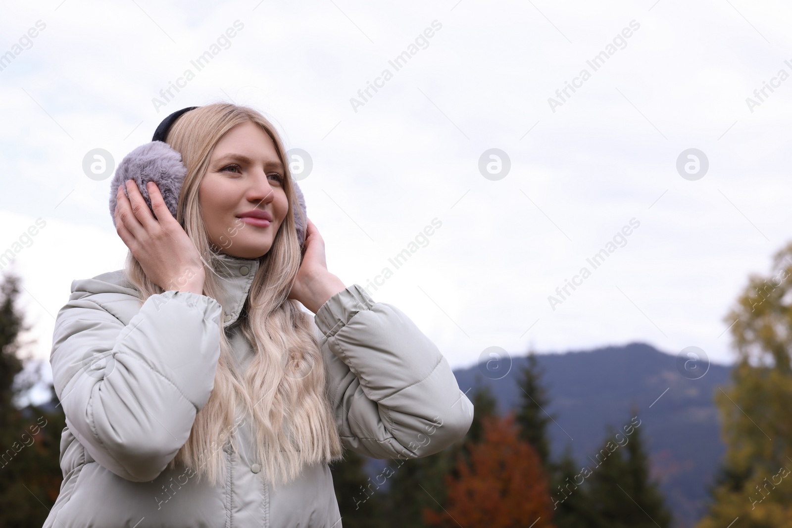 Photo of Young beautiful woman wearing warm earmuffs in mountains