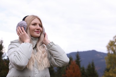 Photo of Young beautiful woman wearing warm earmuffs in mountains