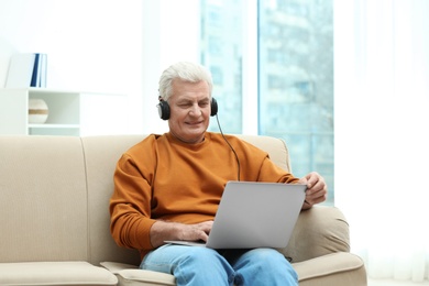 Portrait of mature man with laptop and headphones on sofa indoors