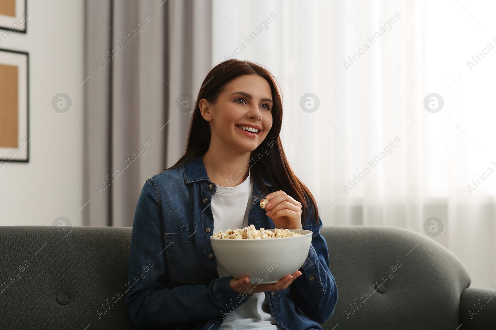 Photo of Happy woman with bowl of popcorn watching TV at home