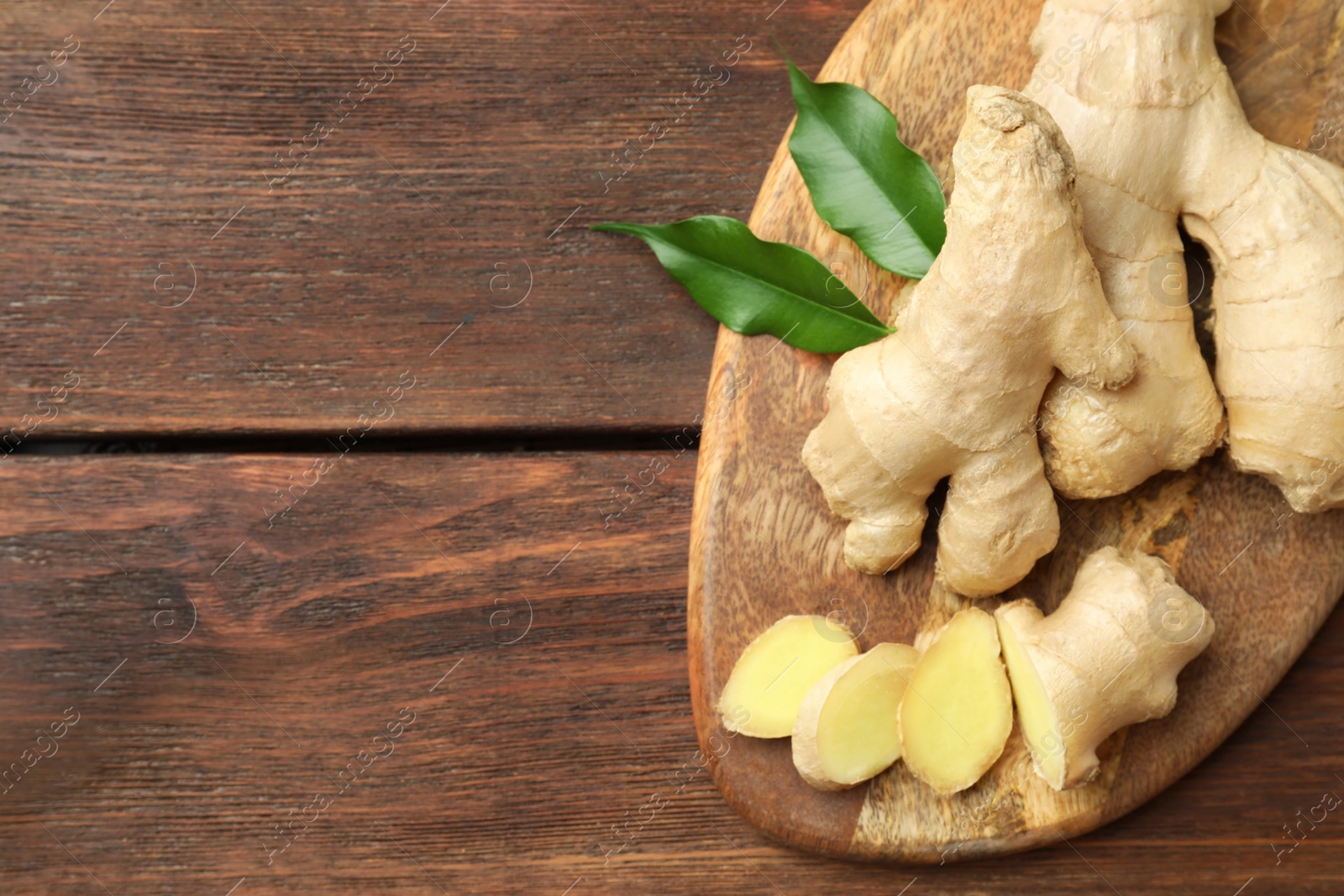 Photo of Cut and whole fresh ginger with leaves on wooden table, top view. Space for text