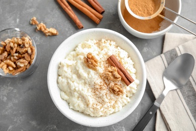 Photo of Creamy rice pudding with cinnamon and walnuts in bowl served on grey table, top view