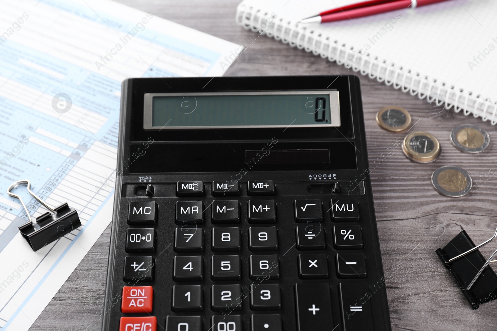 Photo of Tax accounting. Calculator, document, stationery and coins on wooden table, closeup