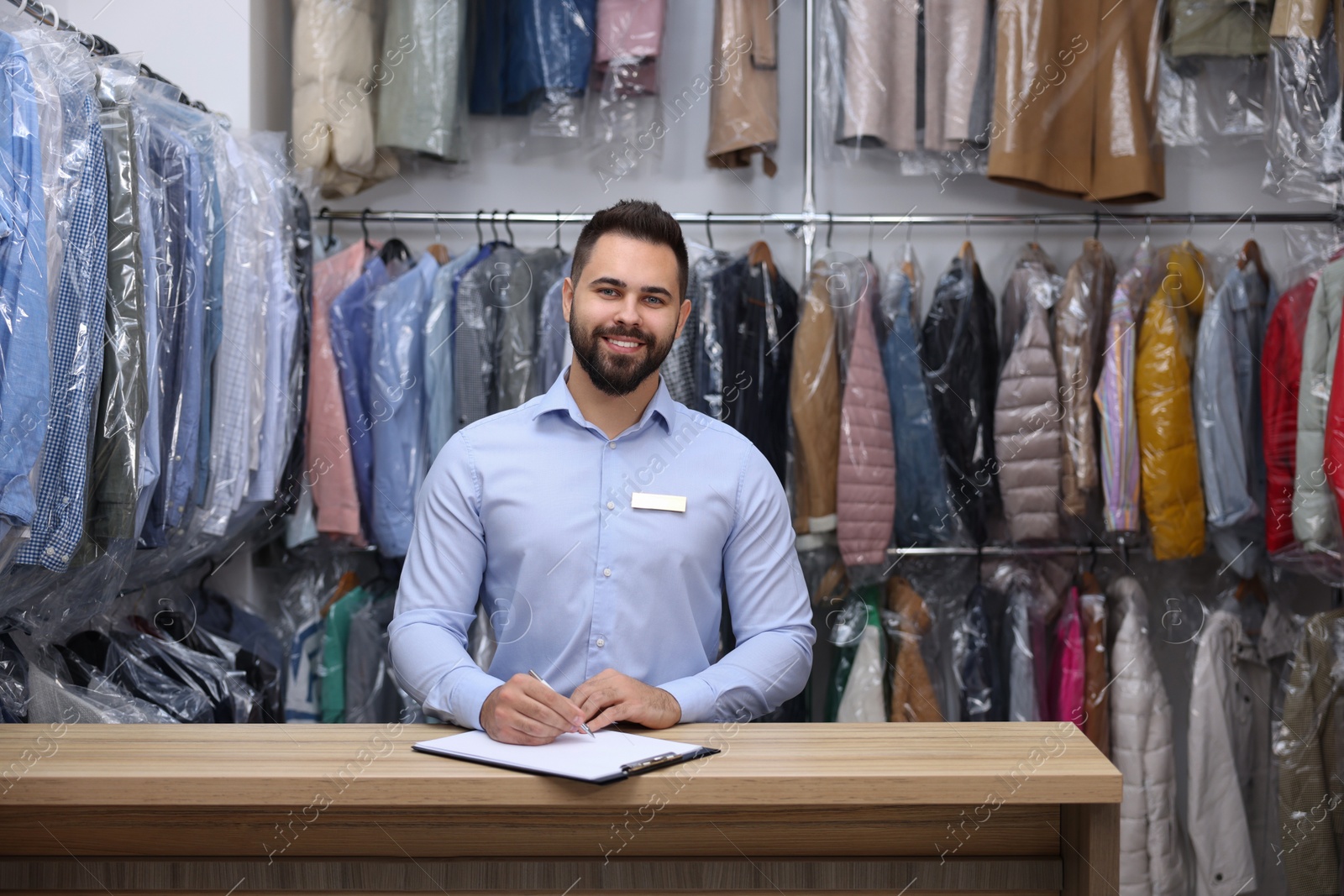 Photo of Dry-cleaning service. Happy worker at counter indoors