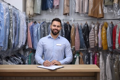 Dry-cleaning service. Happy worker at counter indoors