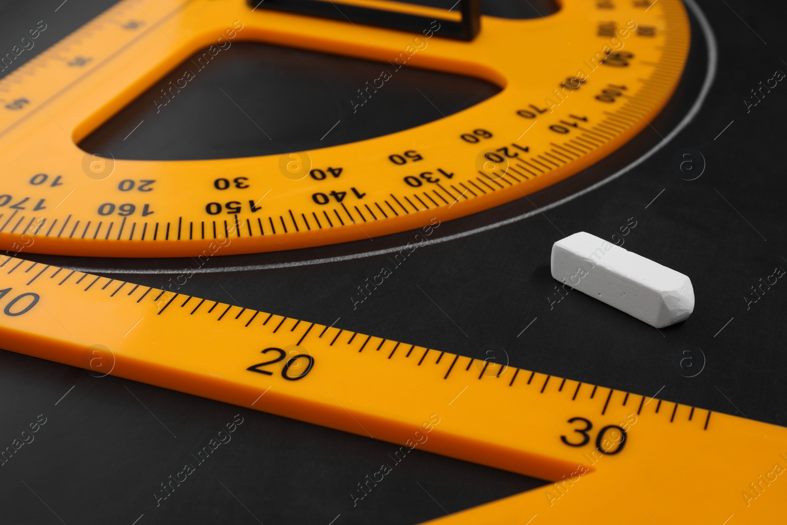 Photo of Protractor, chalk and triangle ruler on blackboard, closeup