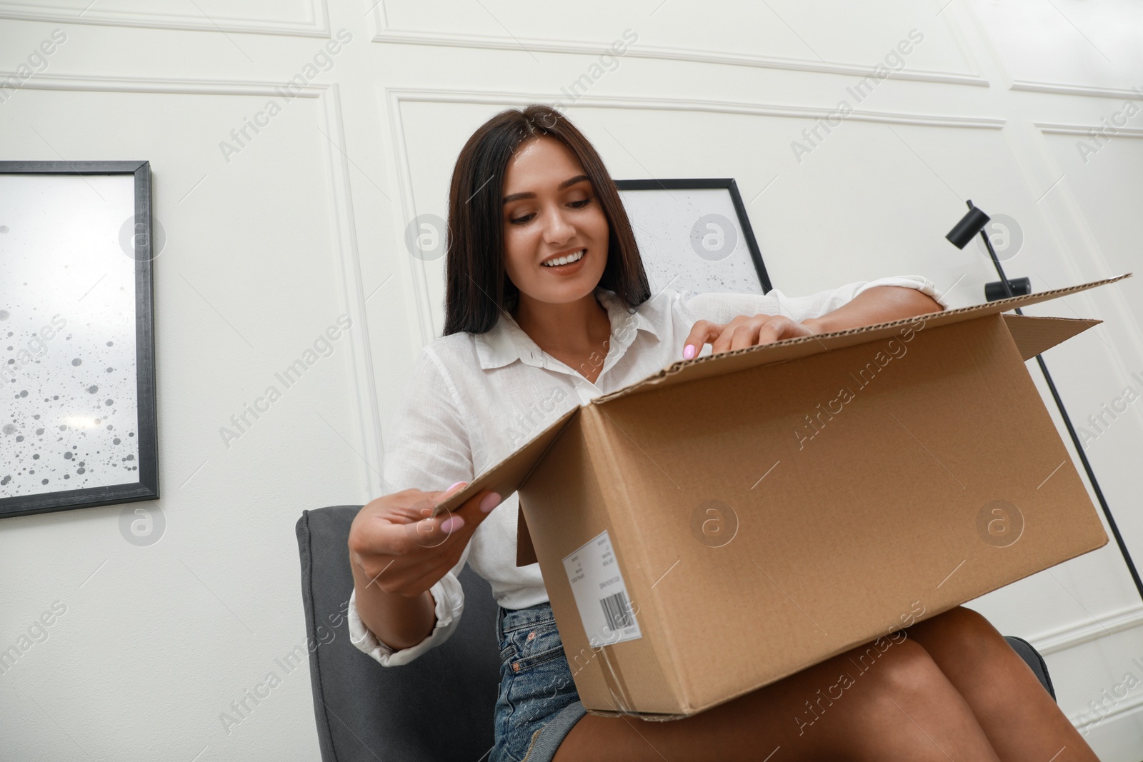 Photo of Happy young woman opening parcel at home. Internet shopping