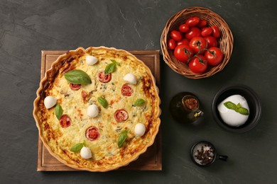 Photo of Delicious homemade cheese quiche and ingredients on black table, flat lay