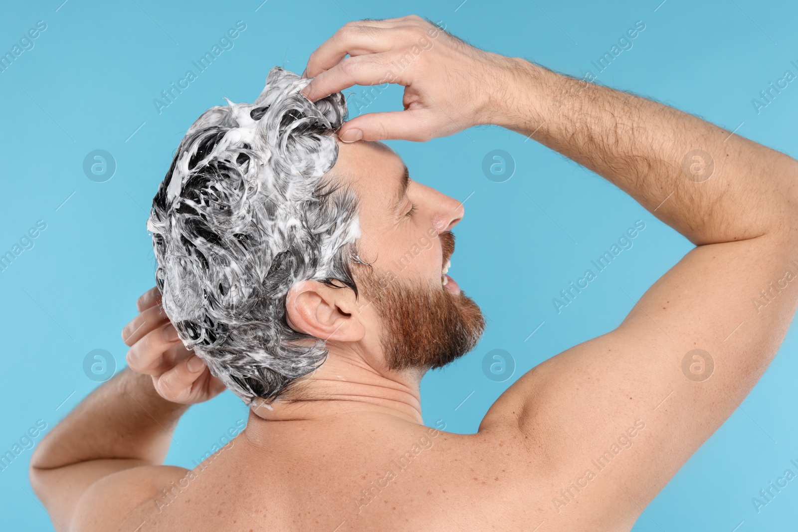 Photo of Man washing his hair with shampoo on light blue background, back view