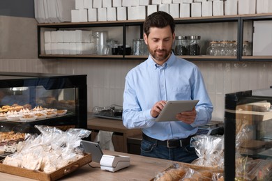 Photo of Smiling business owner with tablet at cashier desk in bakery shop