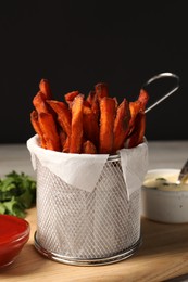 Photo of Frying basket with sweet potato fries, sauces and parsley on table