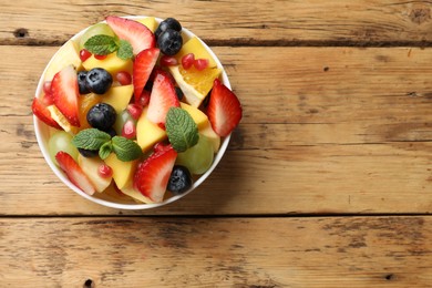 Tasty fruit salad in bowl on wooden table, top view. Space for text