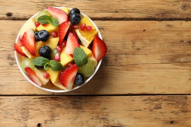 Photo of Tasty fruit salad in bowl on wooden table, top view. Space for text