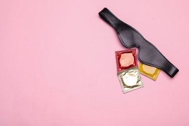 Leather mask and condoms on pink background, top view with space for text. Sex game