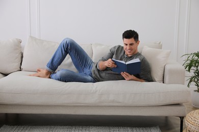 Photo of Man with book lying on comfortable sofa in living room