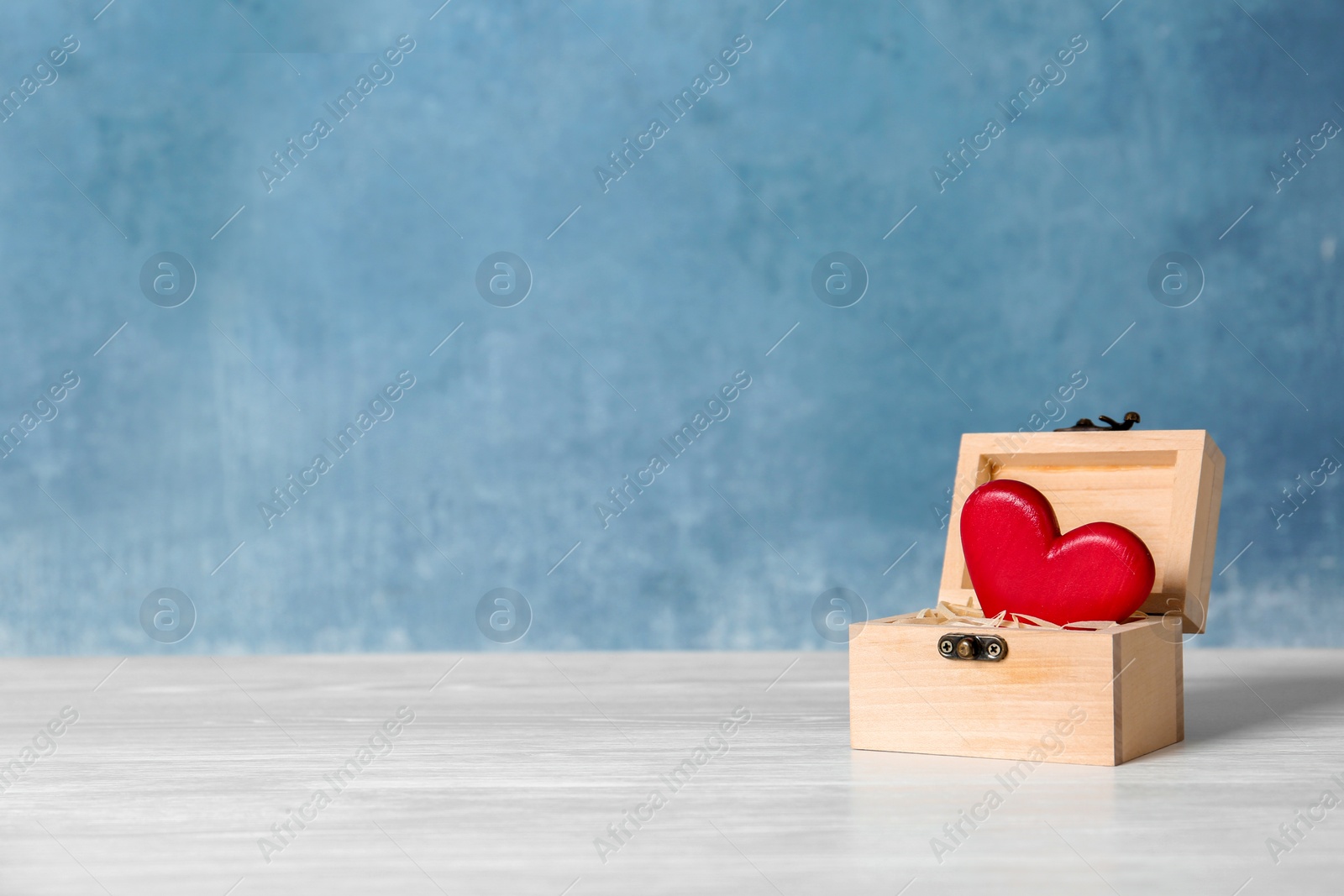 Photo of Small wooden chest with red decorative heart on table. Space for text