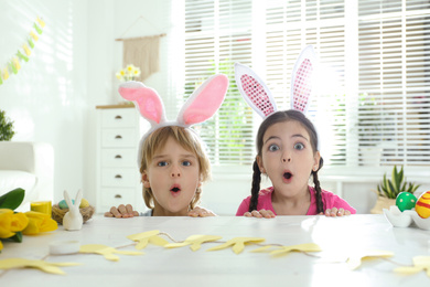 Emotional children wearing bunny ears headbands at table with Easter eggs, indoors