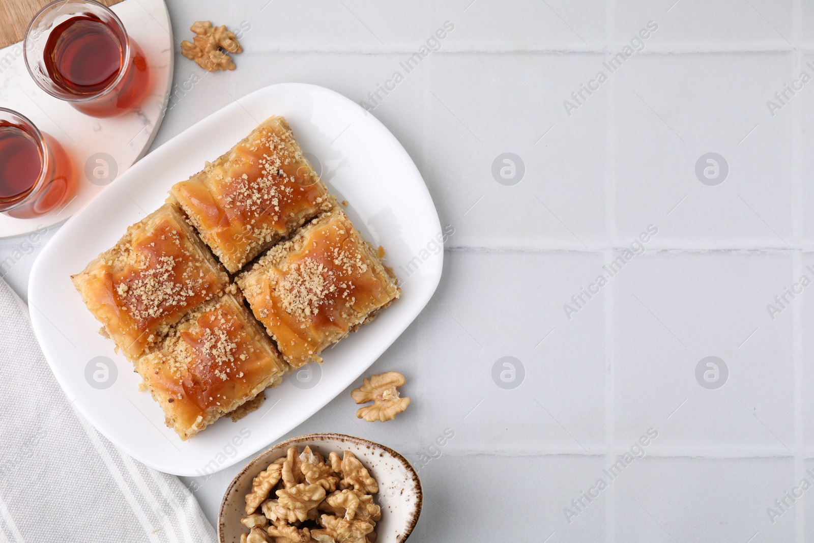 Photo of Eastern sweets. Pieces of tasty baklava, walnuts and tea on white tiled table, flat lay. Space for text