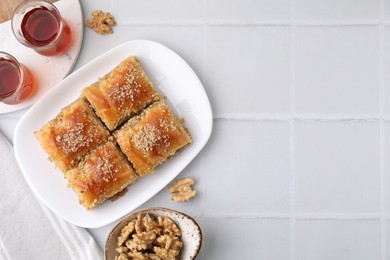 Photo of Eastern sweets. Pieces of tasty baklava, walnuts and tea on white tiled table, flat lay. Space for text