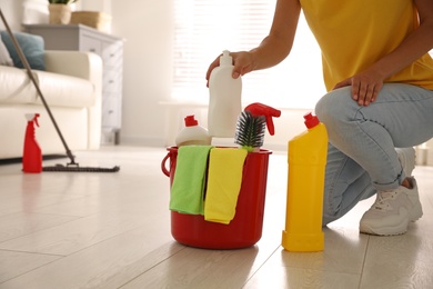 Photo of Woman holding bucket with cleaning supplies in living room, closeup