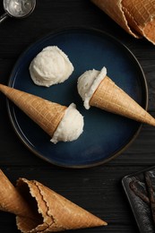 Ice cream scoops in wafer cones on black wooden table, flat lay