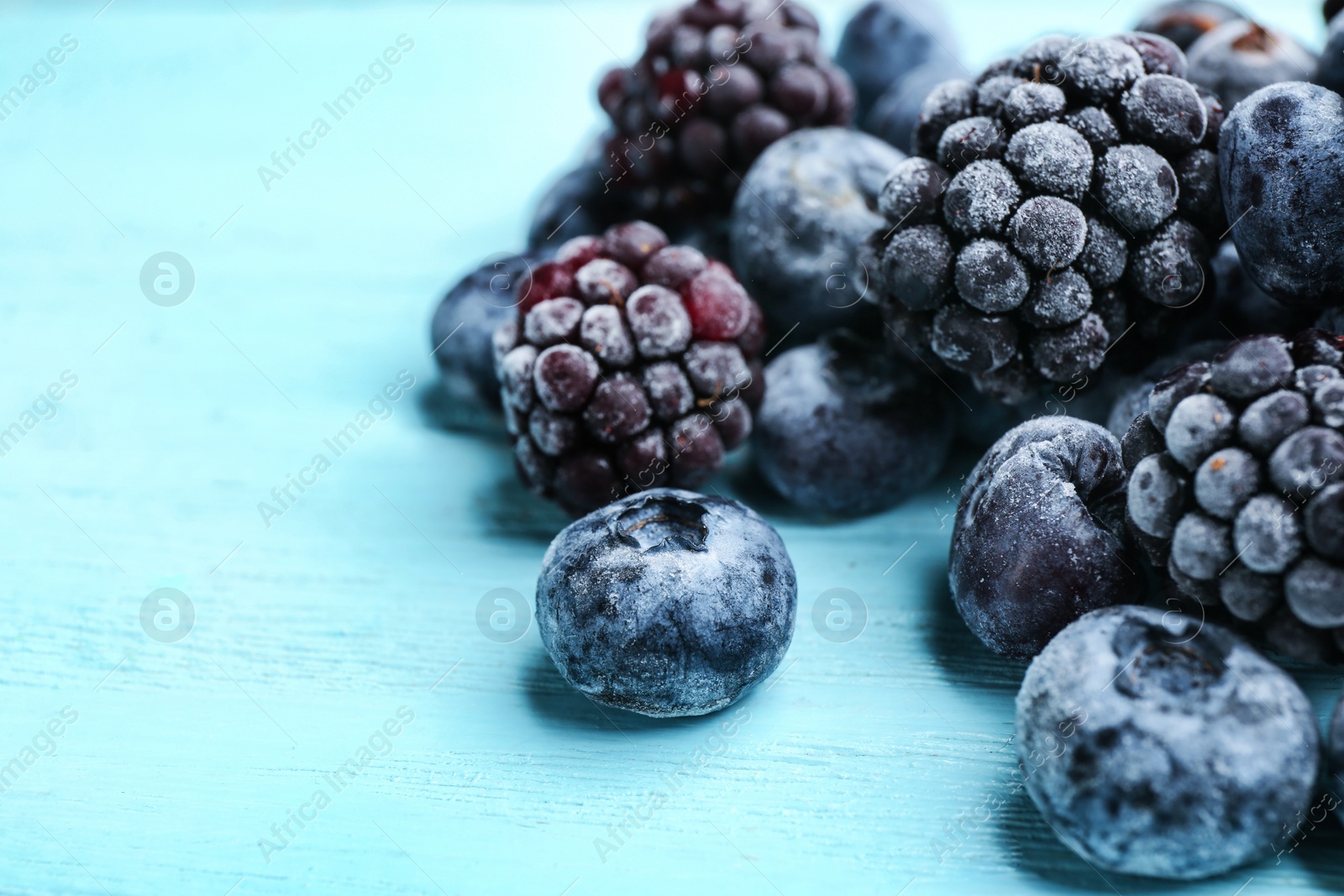 Photo of Tasty frozen blackberries and blueberries on light blue wooden table, closeup. Space for text