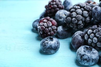 Tasty frozen blackberries and blueberries on light blue wooden table, closeup. Space for text